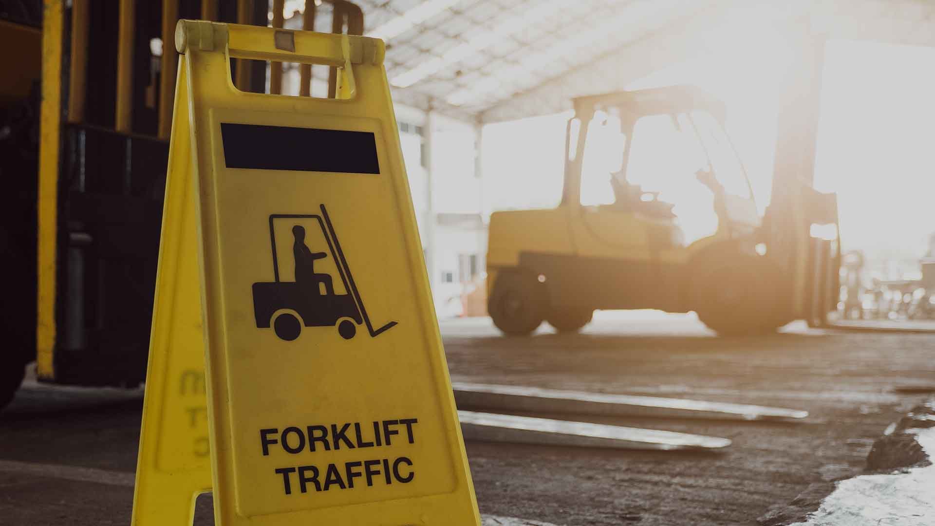 Yellow forklift traffic safety sign with a forklift sitting in the background
