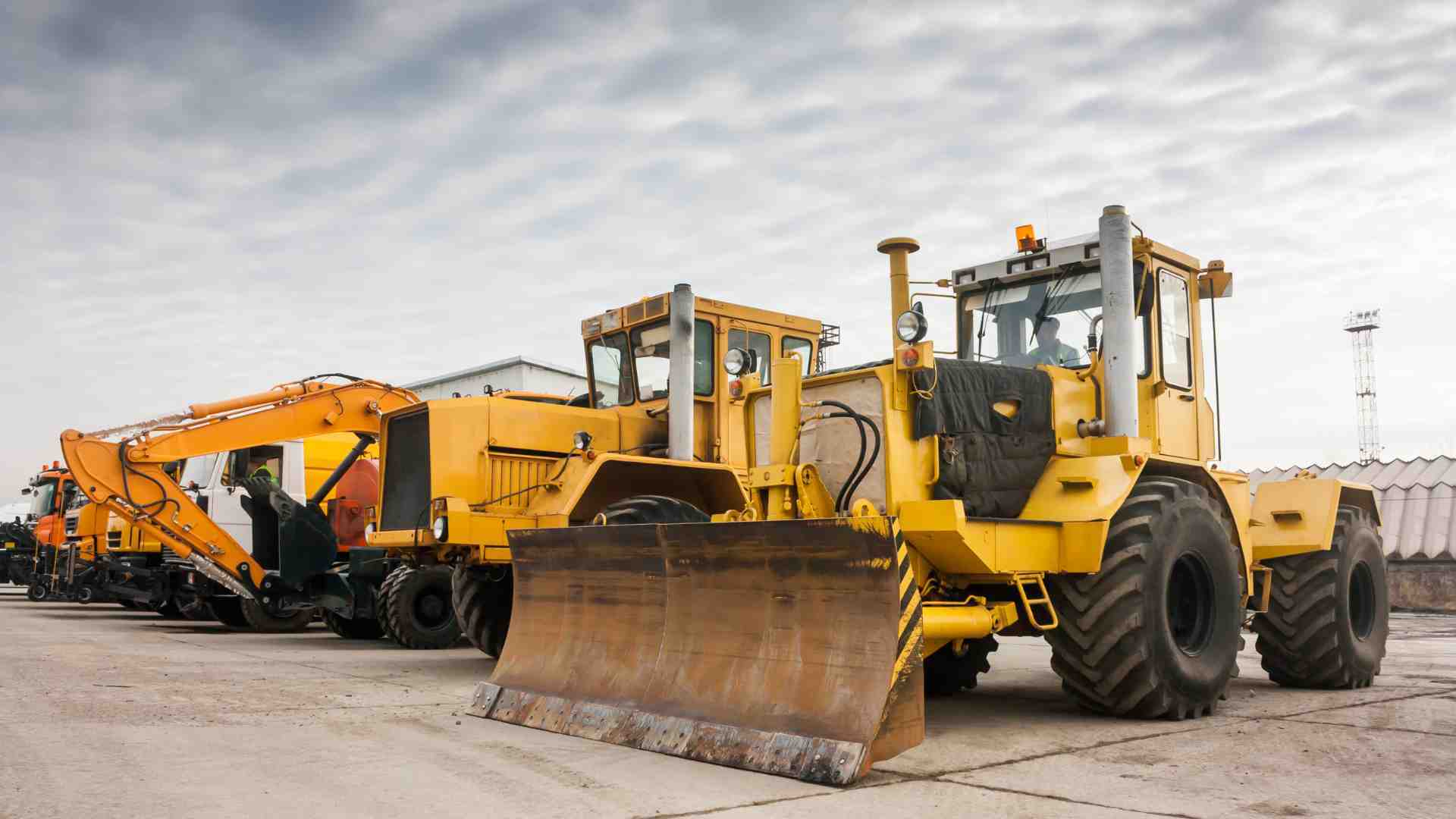 Various heavy, yellow machinery parked side-by-side in a yard