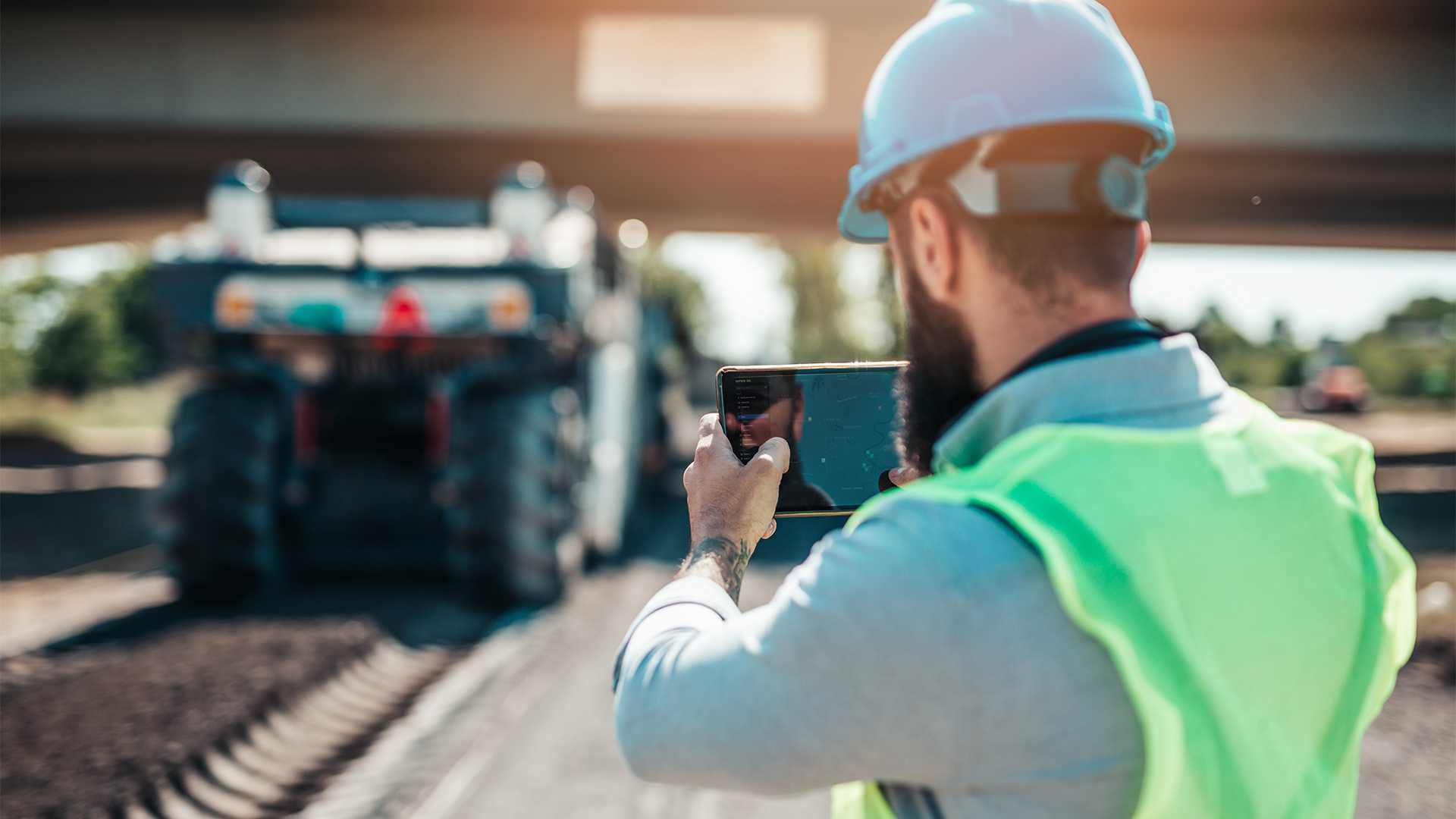 Close up of a man with a device inspecting a heavy machine in the background