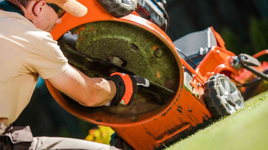 Close up of a man maintaining the blades underneath a lawn mower